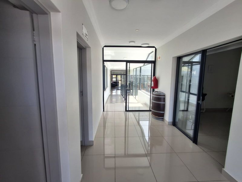 A bright, modern hallway featuring polished tiled flooring and aluminium-framed glass doors leading to an adjacent space.