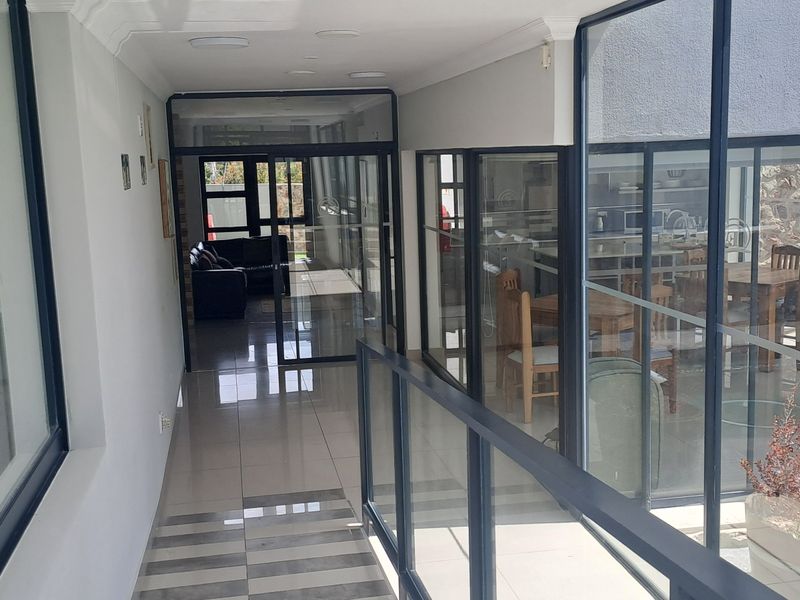 A bright, modern hallway featuring extensive glass partitioning, tiled flooring, and a metal balustrade, providing clear views into adjacent living and dining areas.