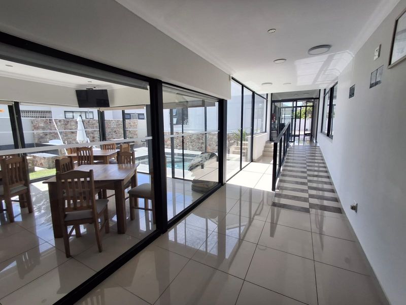 A bright, modern hallway featuring large glass sliding doors that provide a view of the outdoor pool area and tiled flooring throughout.