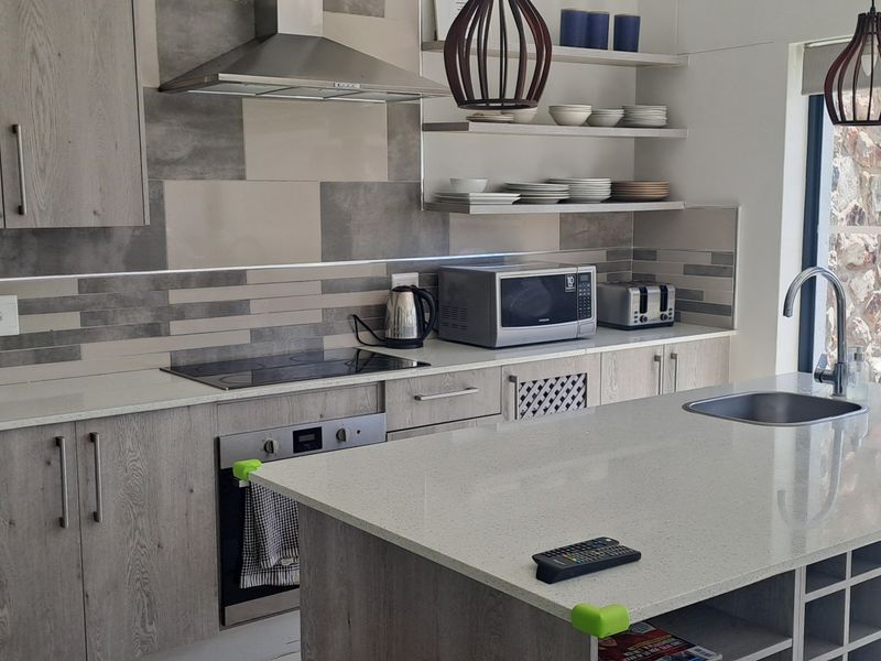 Modern kitchen featuring light wood-grain cabinetry, stone countertops, a central island with integrated sink, and high-quality built-in appliances.