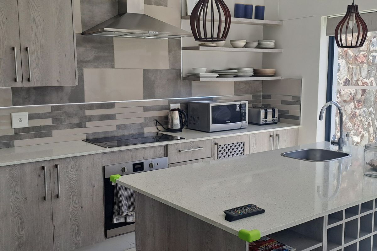 Modern kitchen featuring light wood-grain cabinetry, stone countertops, a central island with integrated sink, and high-quality built-in appliances.
