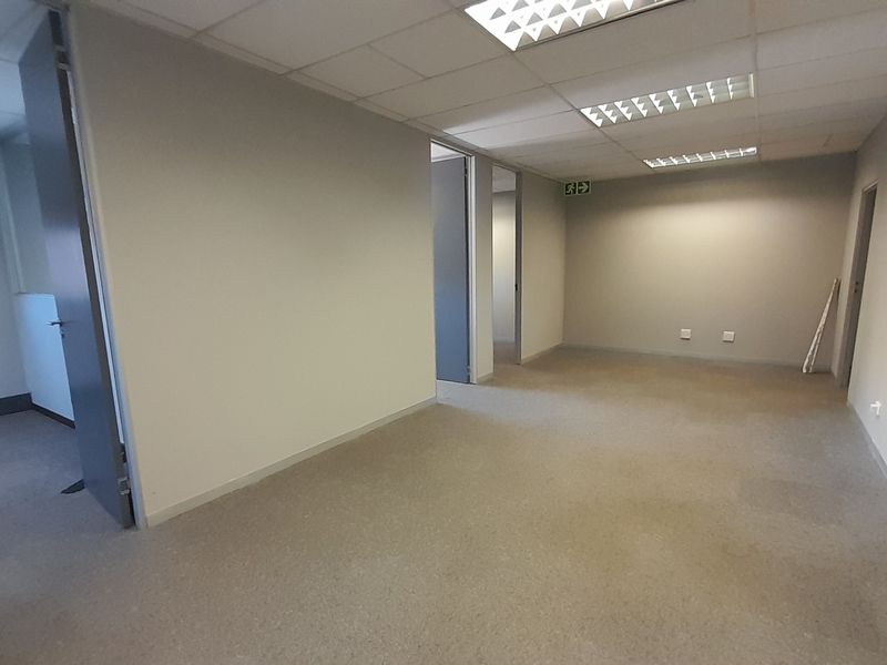 A spacious, empty office suite featuring neutral walls, carpeted flooring, and a suspended ceiling with recessed lighting, offering a clean and versatile workspace.