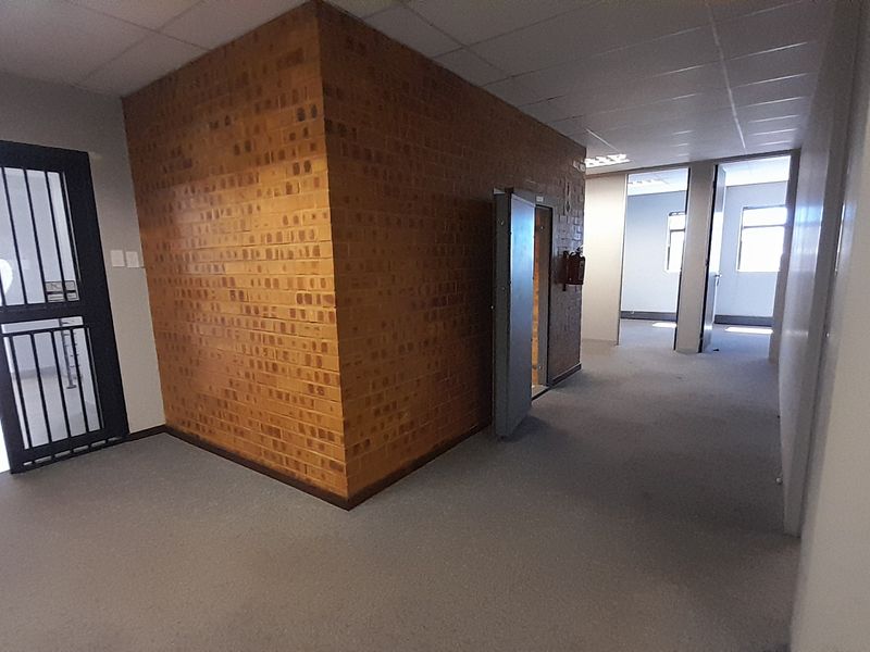 An open-plan office space featuring an exposed brick wall, suspended ceiling, and secure entrance gate, providing a functional and versatile workspace.