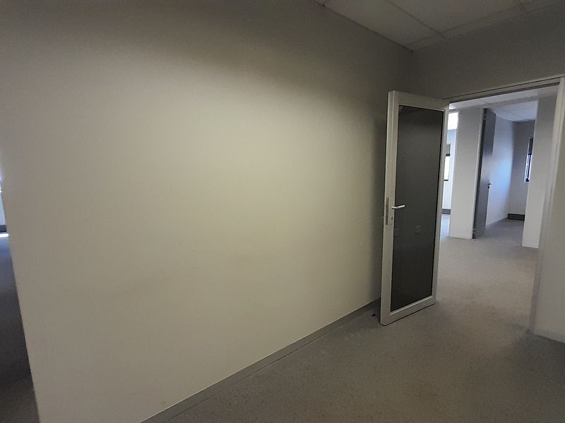 An empty office space featuring neutral walls, carpeted flooring, and a suspended ceiling, providing a clean and versatile work environment.