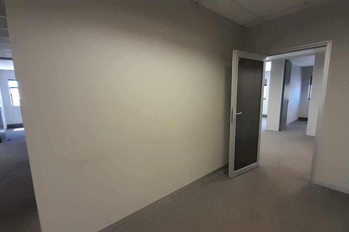 An empty office space featuring neutral walls, carpeted flooring, and a suspended ceiling, providing a clean and versatile work environment.