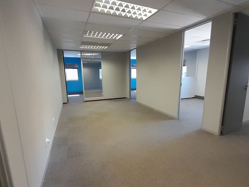 A vacant, open-plan office space featuring neutral carpeting, suspended ceilings with recessed lighting, and multiple internal access points.