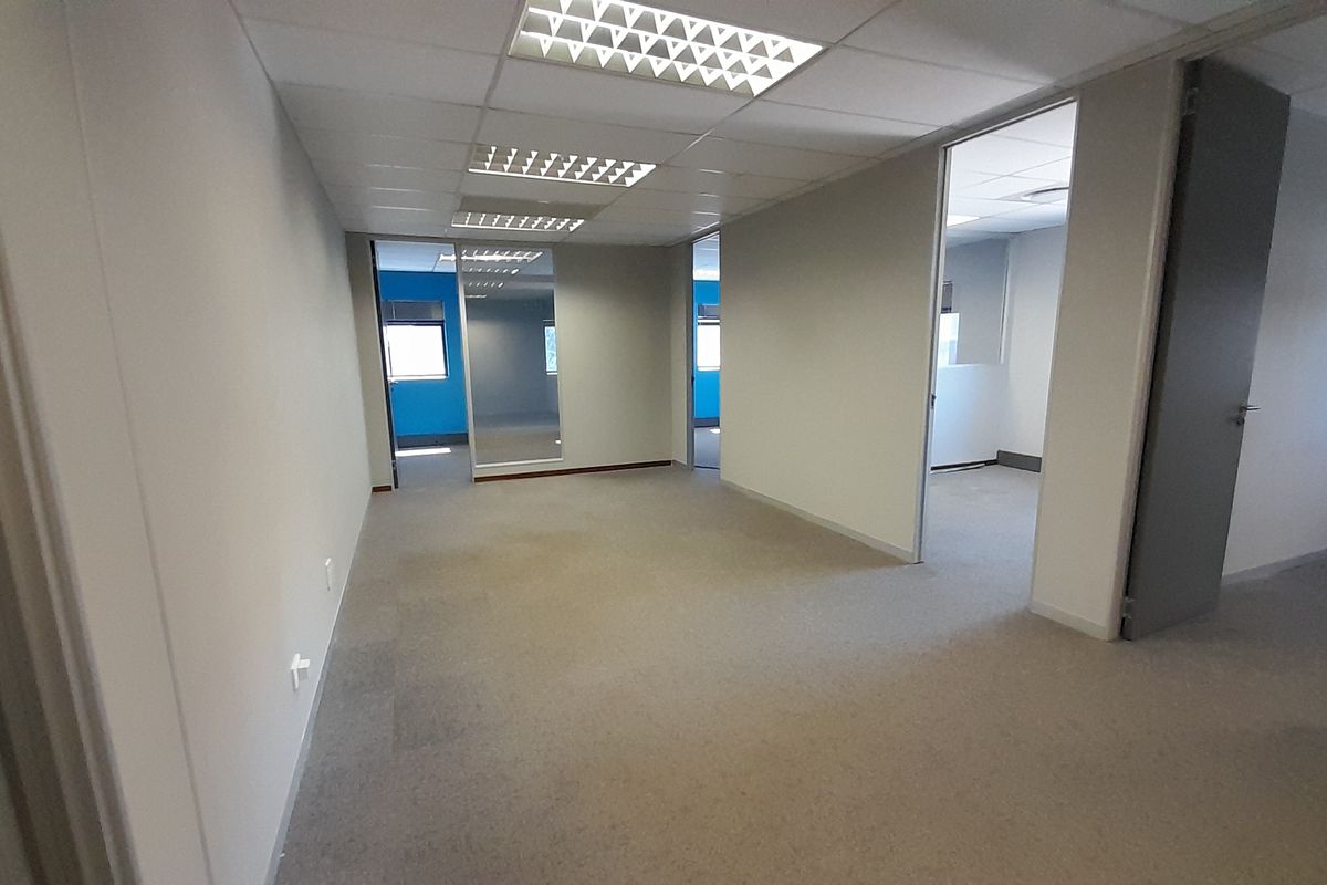 A vacant, open-plan office space featuring neutral carpeting, suspended ceilings with recessed lighting, and multiple internal access points.