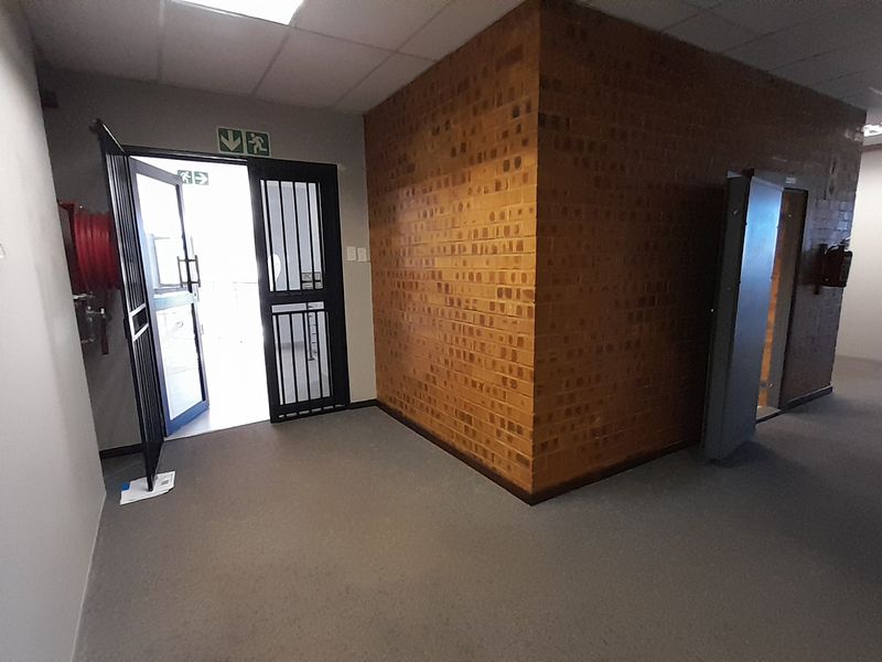 An empty office space featuring an exposed brick feature wall, security gate access, and neutral carpeting in a functional commercial layout.