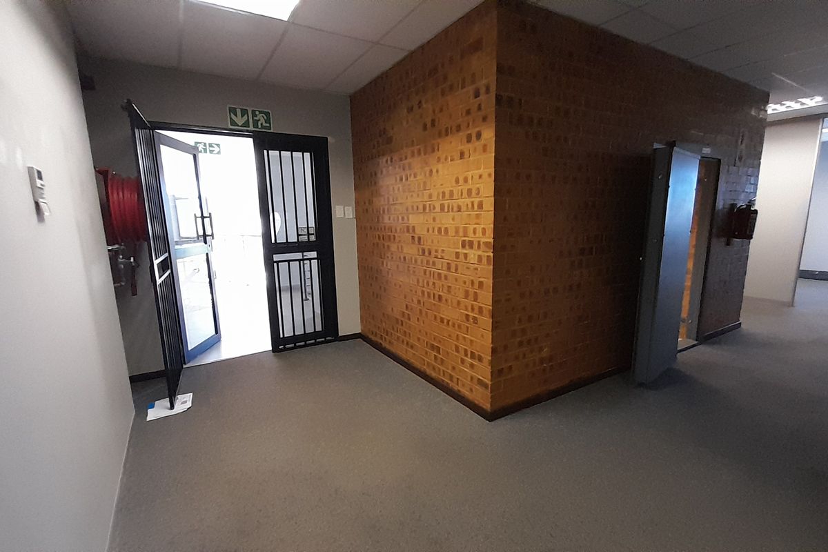 An empty office space featuring an exposed brick feature wall, security gate access, and neutral carpeting in a functional commercial layout.