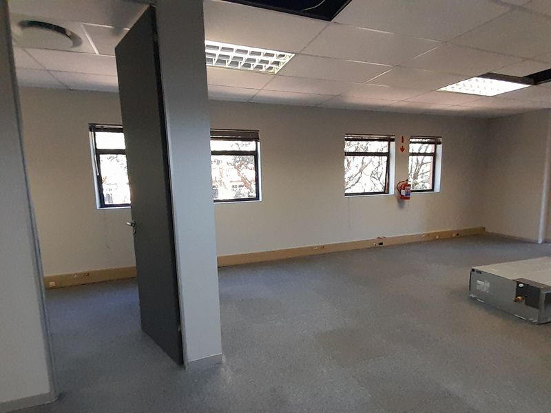 An empty, open-plan office space featuring suspended ceilings, recessed lighting, and vinyl flooring, currently undergoing maintenance with some ceiling tiles missing.