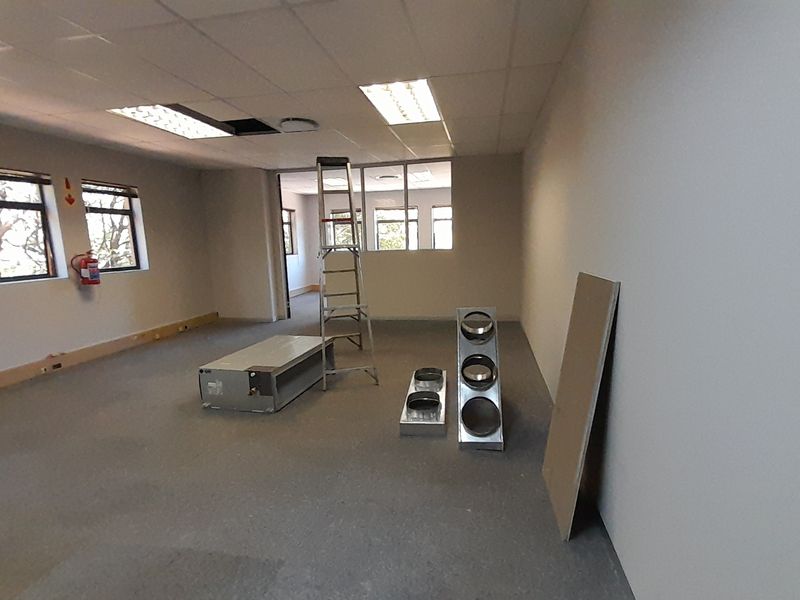 An empty office space featuring a suspended ceiling, recessed lighting, and carpeted flooring, currently undergoing maintenance or renovation.