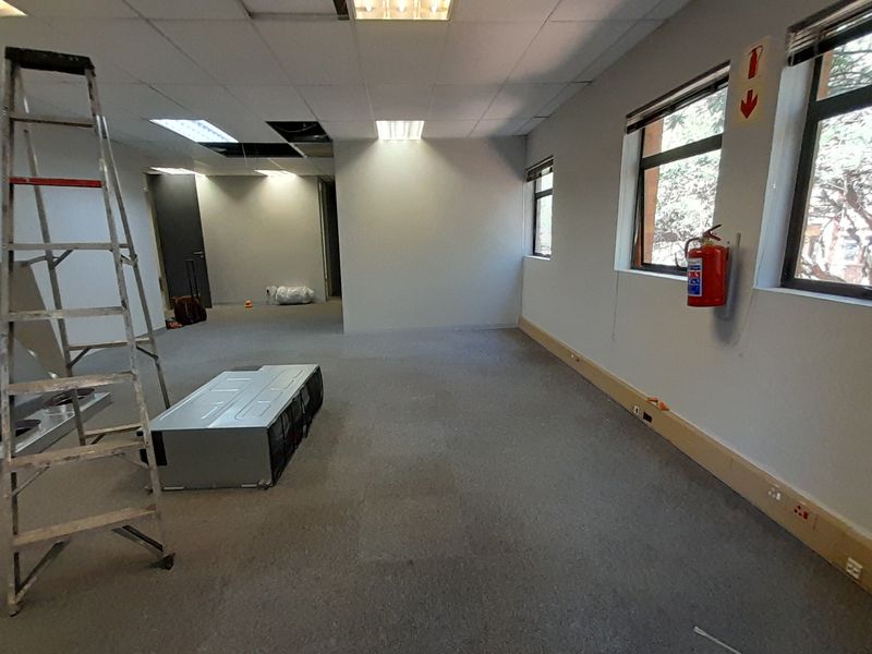 An empty office space featuring a suspended ceiling with missing tiles, carpeted flooring, and wall-mounted electrical trunking.