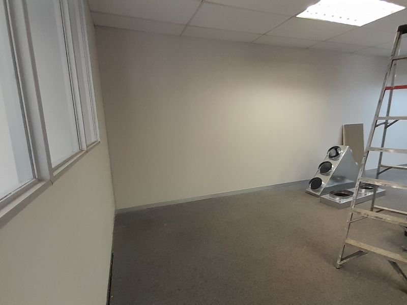 An empty office space featuring a suspended ceiling, recessed lighting, and carpeted flooring, currently undergoing maintenance or minor renovations.