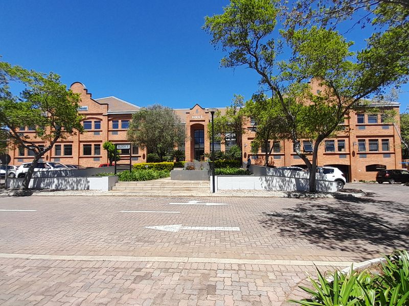 A well-maintained multi-story brick office building featuring a paved entrance area, landscaped gardens, and clear access from the street.