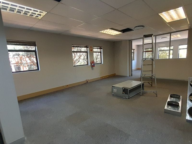 An open-plan office space featuring a suspended ceiling, recessed lighting, and large windows, currently undergoing maintenance with exposed ceiling sections.