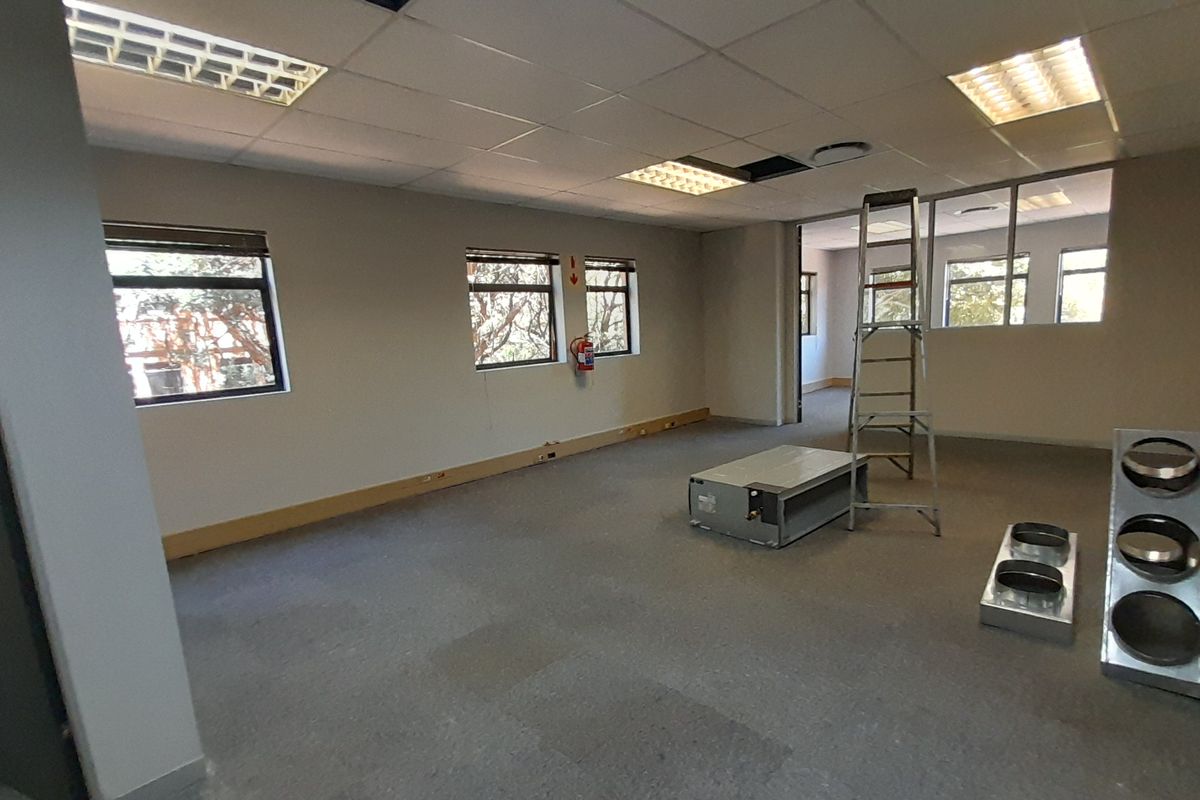 An open-plan office space featuring a suspended ceiling, recessed lighting, and large windows, currently undergoing maintenance with exposed ceiling sections.
