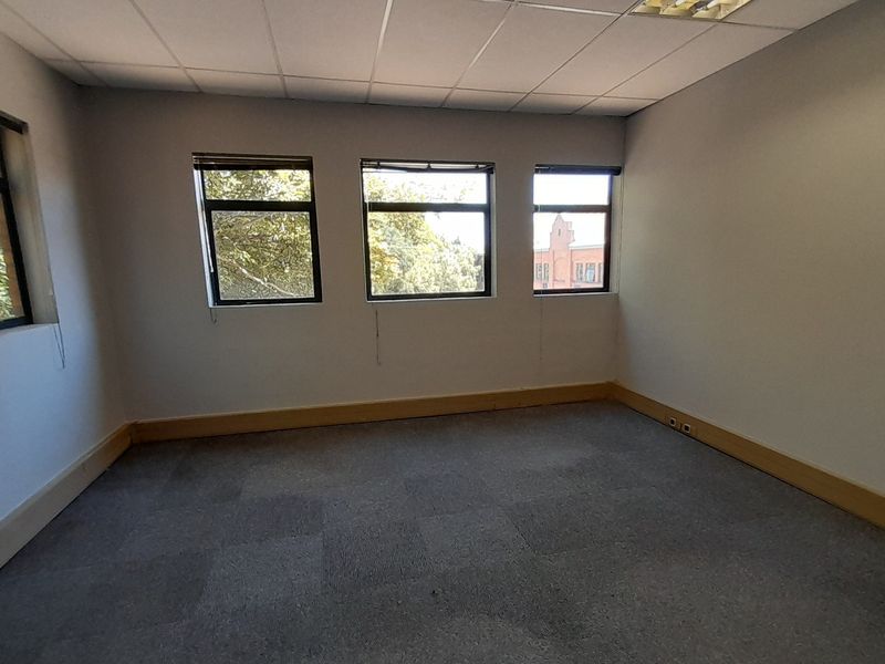 An empty office space featuring carpeted flooring, a suspended ceiling, and multiple windows providing natural light.