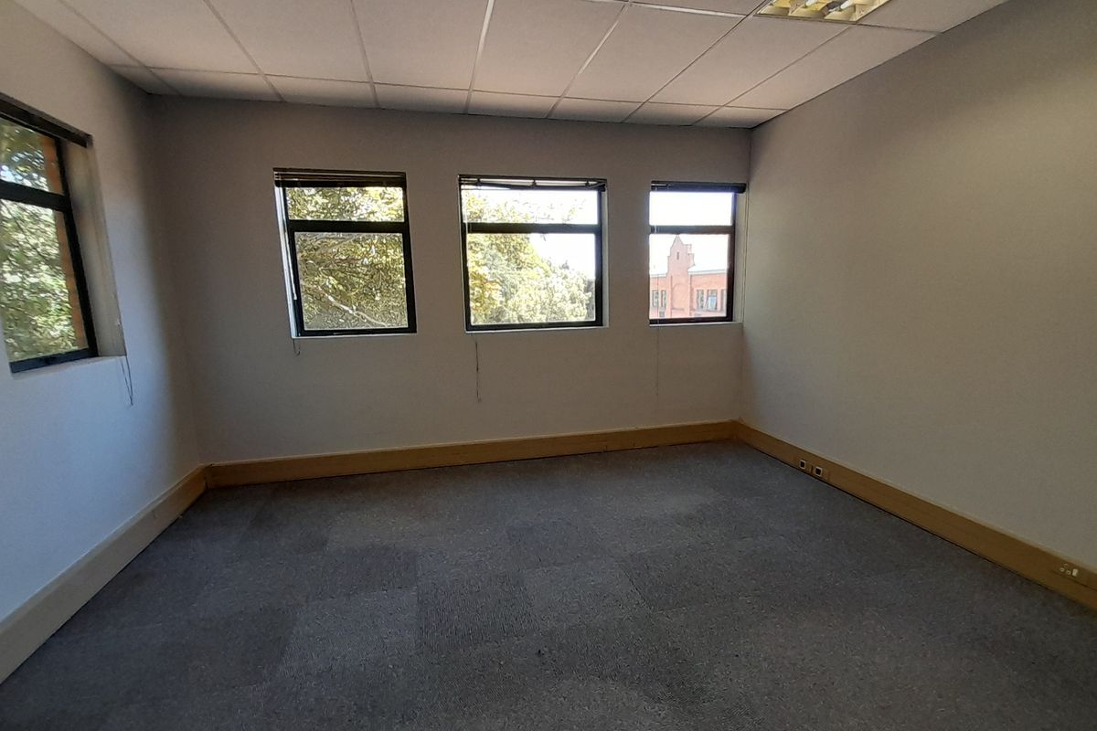 An empty office space featuring carpeted flooring, a suspended ceiling, and multiple windows providing natural light.