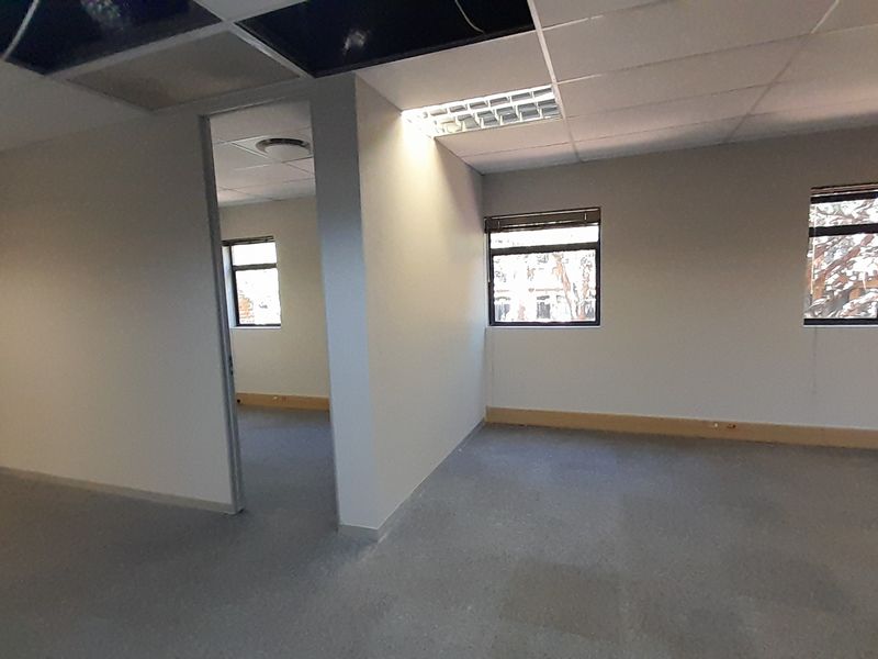 An empty office space featuring carpeted flooring, recessed lighting, and large windows, currently requiring ceiling repairs.
