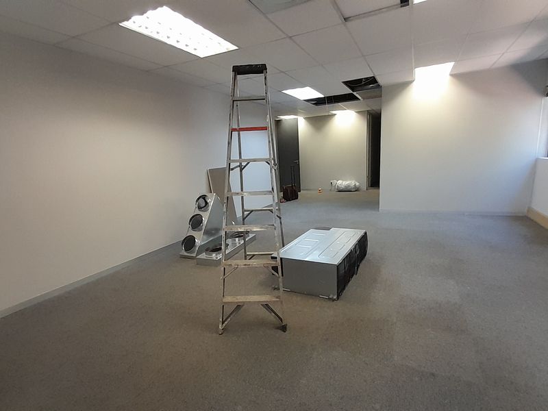 An empty office space featuring a suspended ceiling with recessed lighting and carpeted flooring, currently undergoing maintenance with missing ceiling tiles.