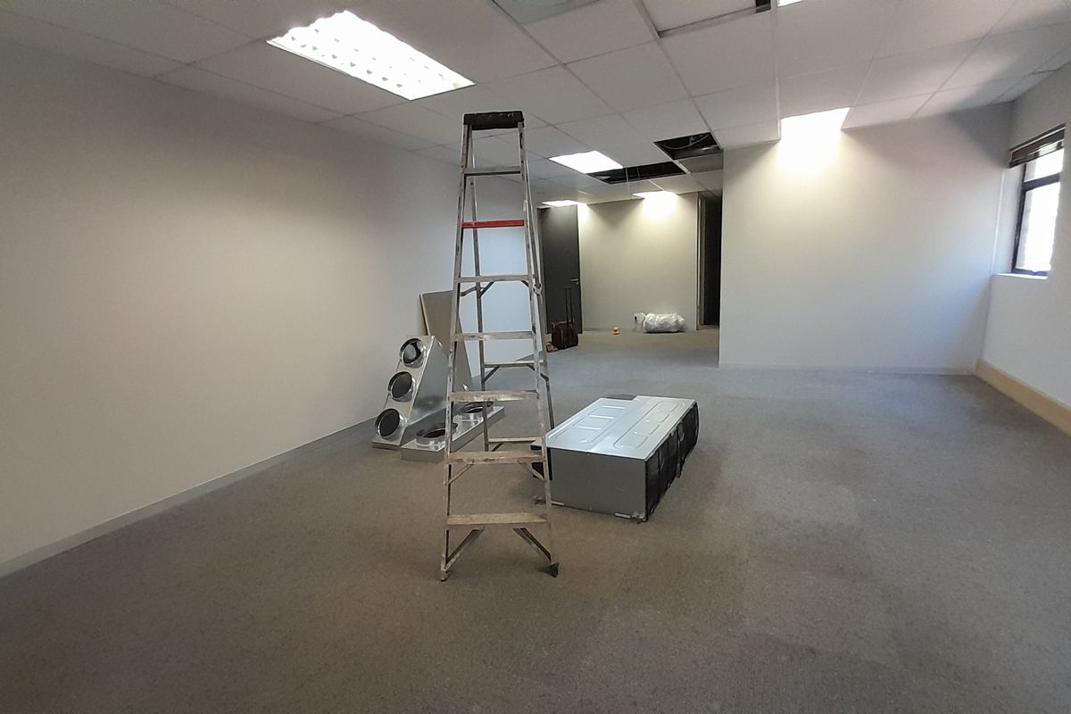 An empty office space featuring a suspended ceiling with recessed lighting and carpeted flooring, currently undergoing maintenance with missing ceiling tiles.
