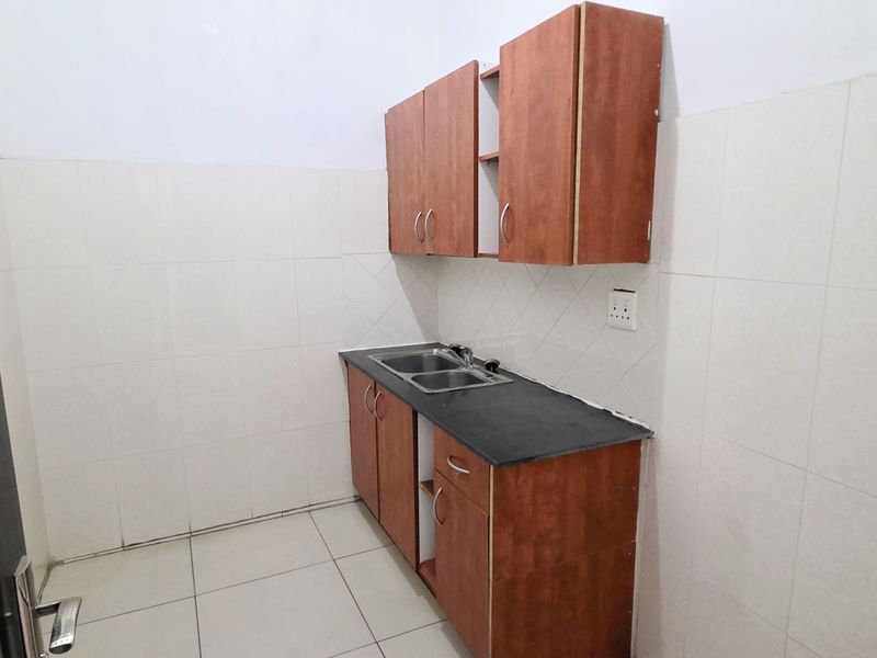 A compact kitchen area featuring built-in wooden cabinetry, a double sink with a stone countertop, and tiled wall finishes.