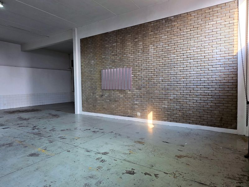 Spacious industrial utility area featuring an exposed brick feature wall, durable concrete flooring, and a large roller shutter door for easy access.