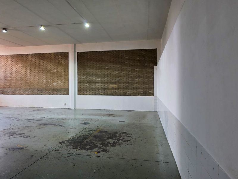 Spacious industrial utility area featuring exposed brick walls, concrete flooring, and recessed ceiling lighting, suitable for storage or workshop use.