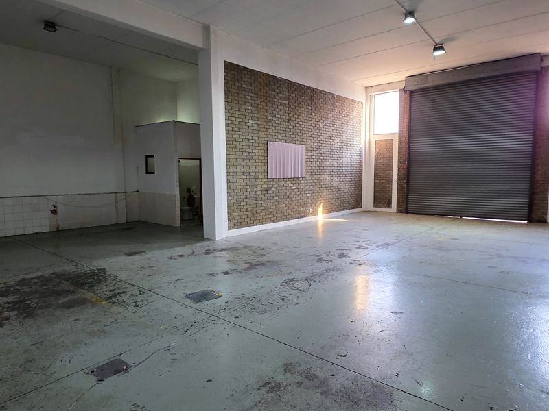Spacious industrial utility area featuring high ceilings, exposed brick walls, durable concrete flooring, and a large roller shutter door for easy access.