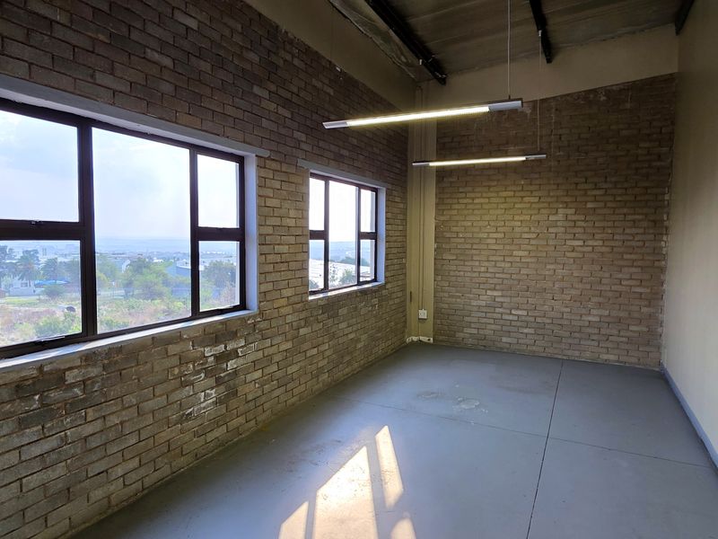 An industrial-style office space featuring exposed brick walls, polished concrete flooring, and large windows providing natural light and elevated views.