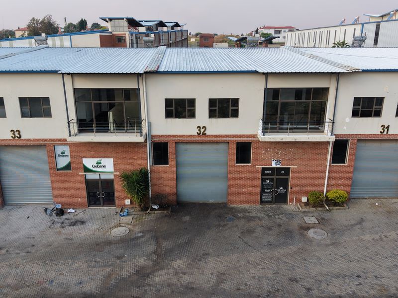 Aerial view of a multi-unit industrial complex featuring brick facades, roller shutter doors, and upper-level balconies with metal roofing.