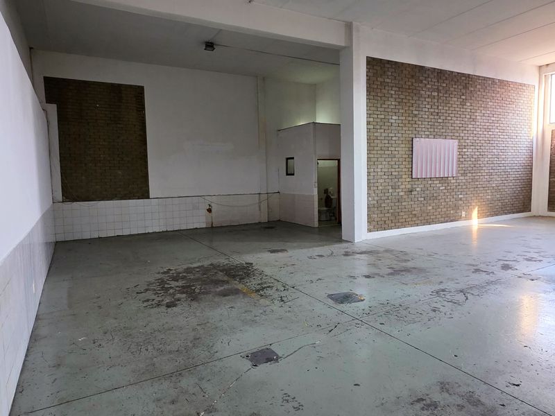 Spacious industrial utility area featuring high ceilings, a large roller shutter door, exposed brickwork, and durable concrete flooring, suitable for various commercial or storage uses.