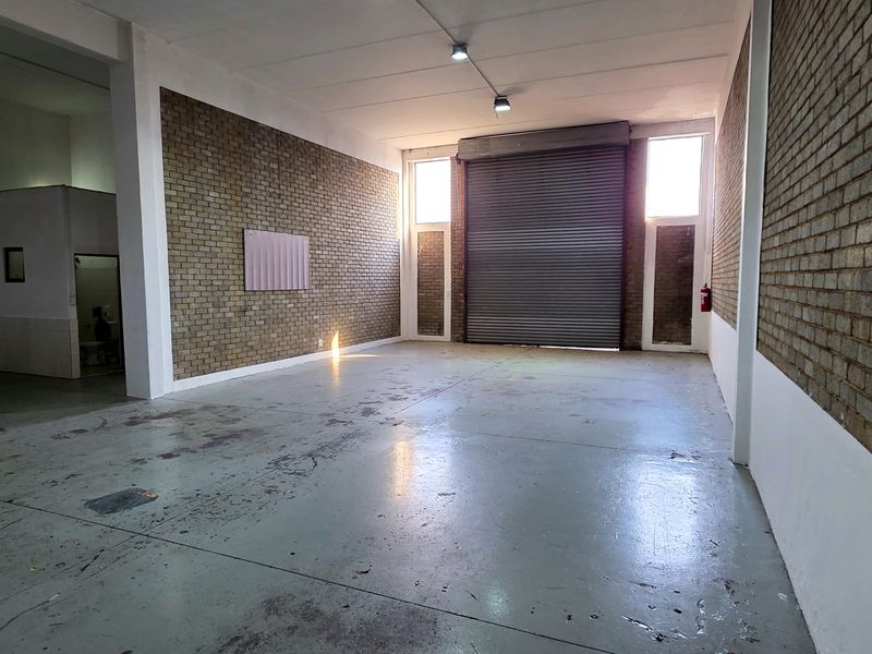 Spacious industrial utility area featuring high ceilings, exposed brick walls, durable concrete flooring, and a large roller shutter door for easy access.