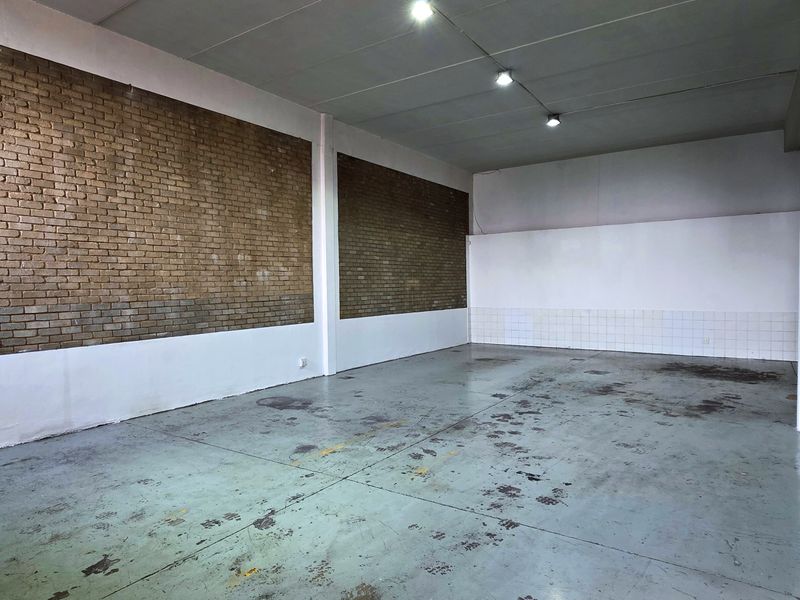 Spacious industrial utility area featuring exposed brick walls, painted concrete flooring, and functional track lighting, suitable for various commercial or storage applications.