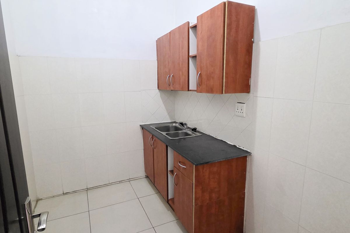 A compact kitchen area featuring built-in wooden cabinetry, a double sink with a stone countertop, and tiled wall finishes.