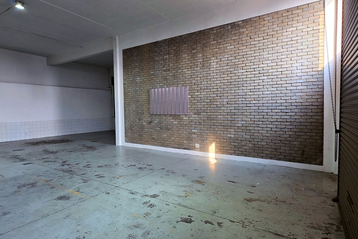 Spacious industrial utility area featuring an exposed brick feature wall, durable concrete flooring, and a large roller shutter door for easy access.