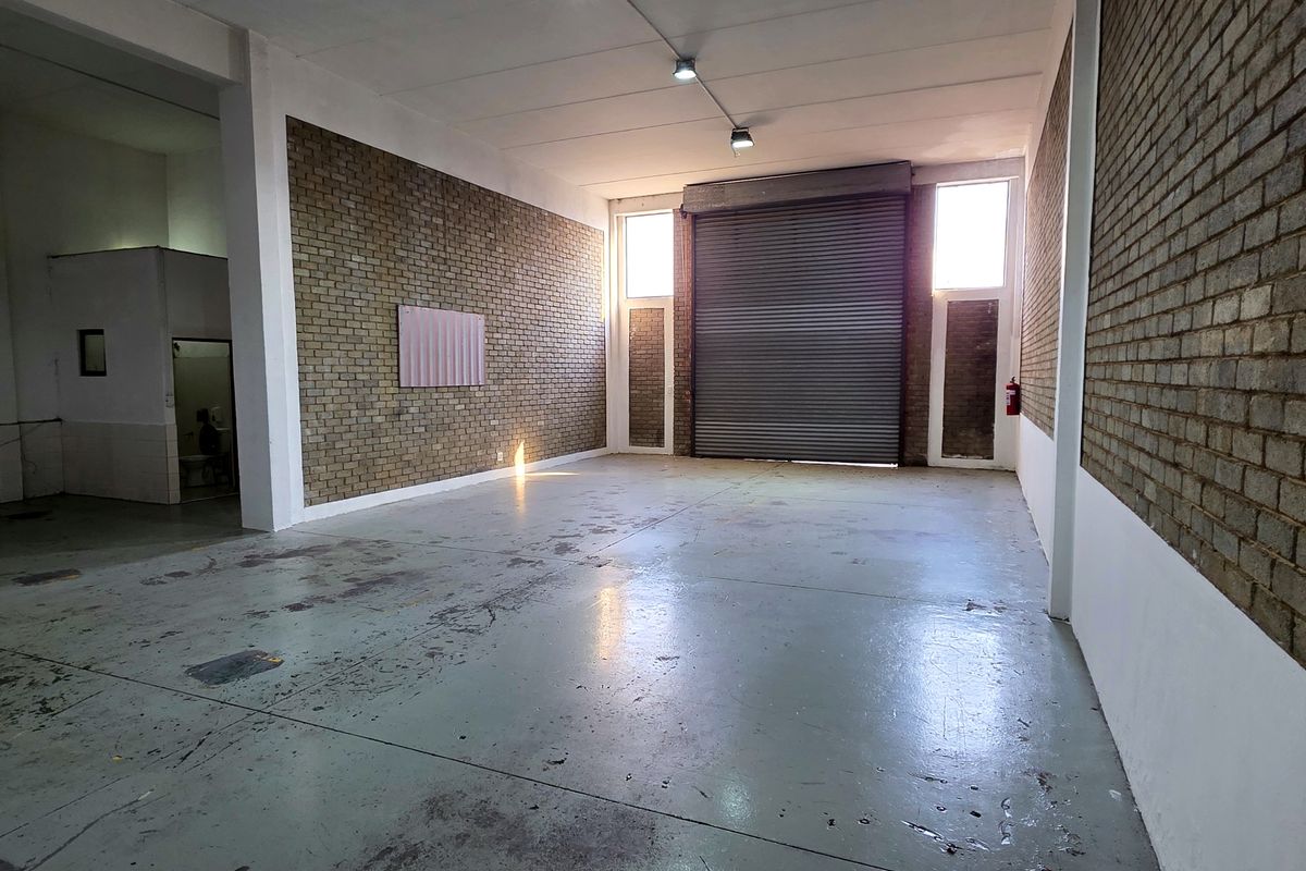 Spacious industrial utility area featuring high ceilings, exposed brick walls, durable concrete flooring, and a large roller shutter door for easy access.
