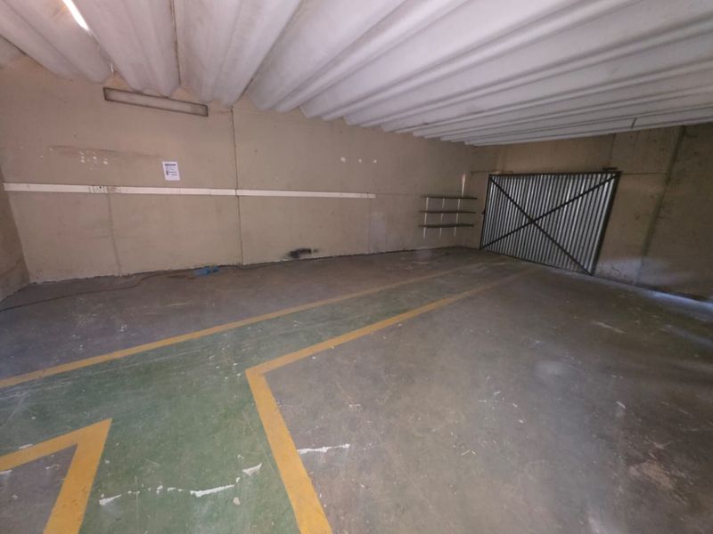 A spacious, utilitarian garage area featuring concrete flooring with painted markings, corrugated metal ceiling, and a secure metal gate entrance.