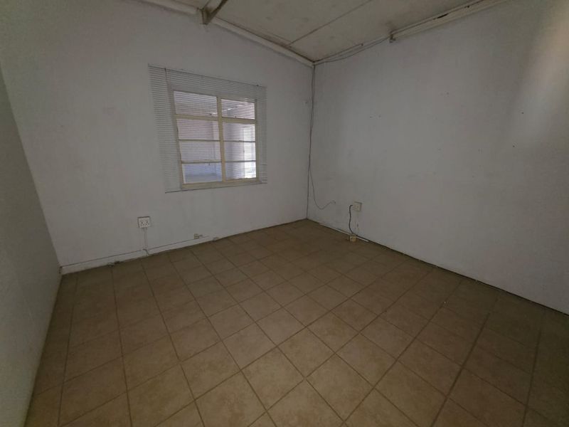 An empty commercial office space featuring tiled flooring, a single window with blinds, and basic electrical points.
