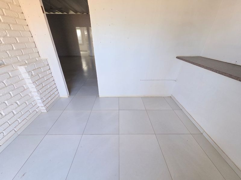 An empty commercial interior space featuring white painted brickwork, tiled flooring, and a built-in service counter.