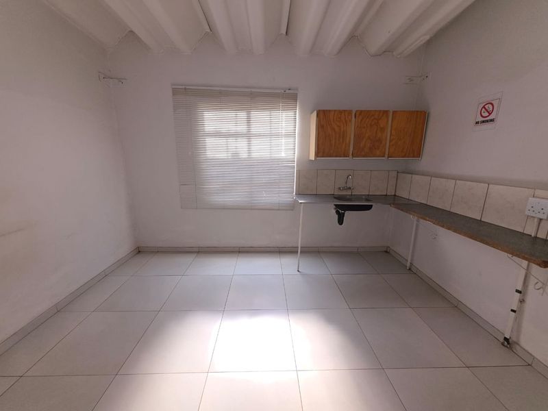 A basic kitchenette area featuring tiled flooring, a simple sink unit with wall-mounted cabinetry, and a window with fitted blinds.