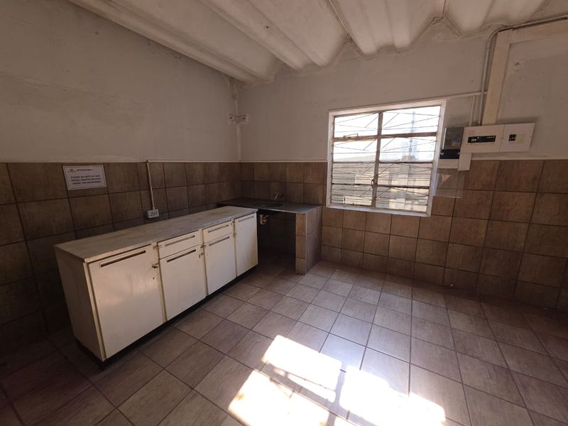 A functional utility or kitchenette area featuring tiled flooring, wall-mounted cabinetry, a sink, and exposed electrical infrastructure.