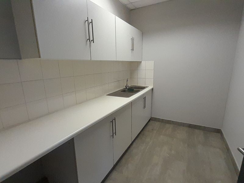 A clean and functional office kitchenette featuring white built-in cabinetry, a stainless steel sink, and durable vinyl flooring.