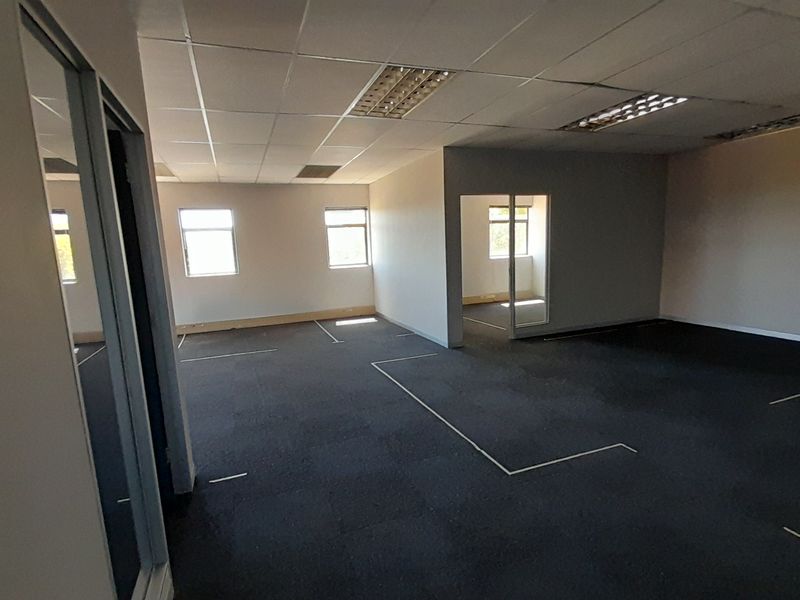 Spacious open-plan office area featuring suspended ceilings, recessed lighting, and dark carpet tiles, offering a versatile layout for professional workspace configuration.