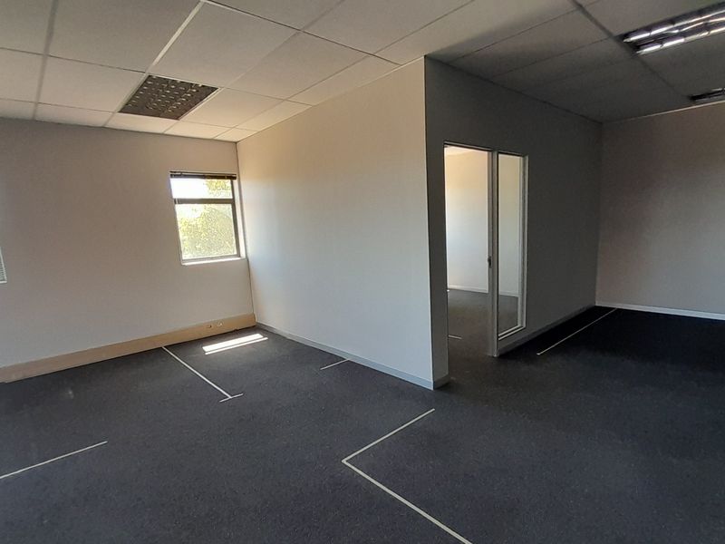 An empty, open-plan office space featuring suspended ceilings, recessed lighting, carpeted flooring, and a glass partition door, offering a versatile workspace layout.