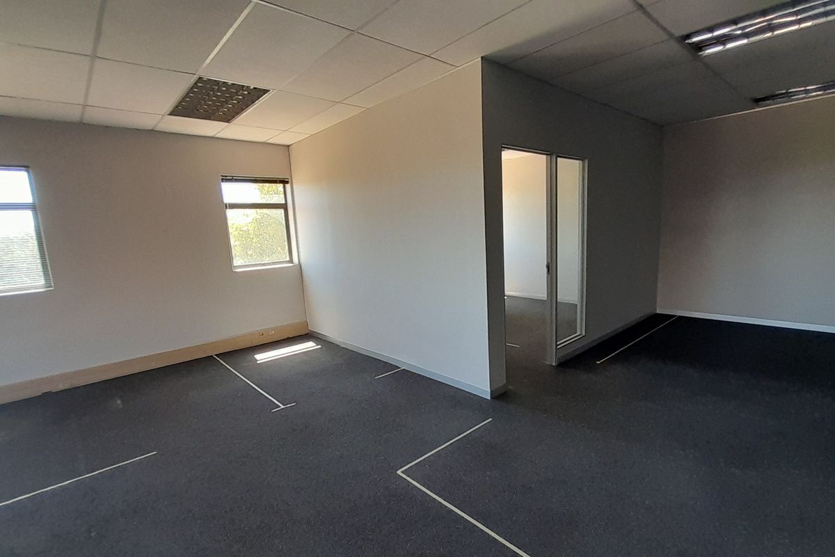 An empty, open-plan office space featuring suspended ceilings, recessed lighting, carpeted flooring, and a glass partition door, offering a versatile workspace layout.