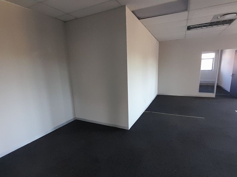 An empty, open-plan office space featuring neutral walls, dark carpeting, and a suspended ceiling with integrated lighting.