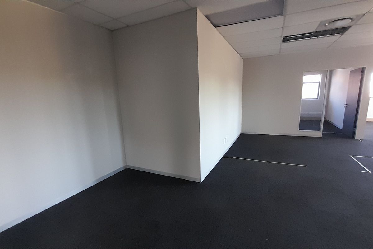 An empty, open-plan office space featuring neutral walls, dark carpeting, and a suspended ceiling with integrated lighting.