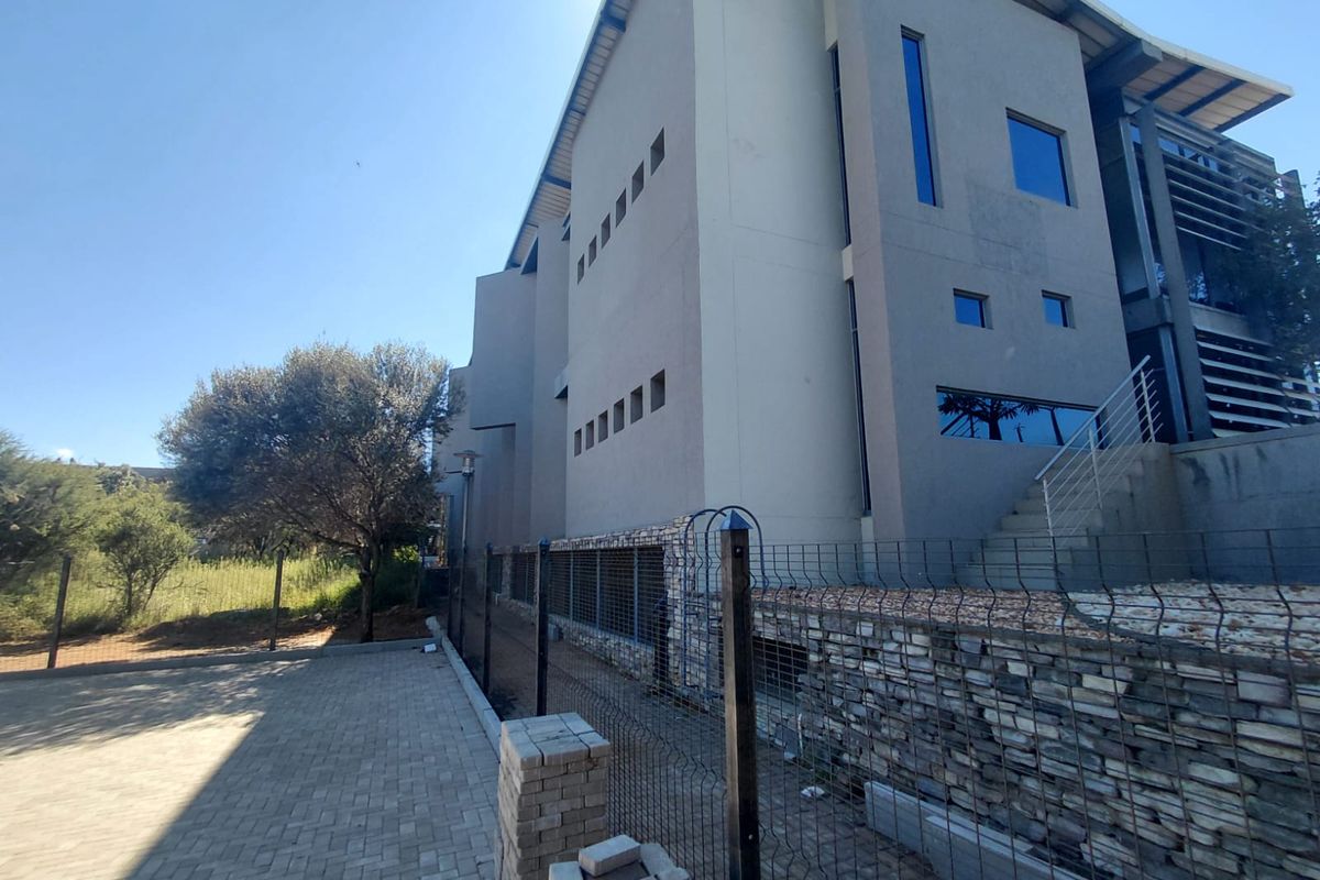Side elevation of a modern commercial building featuring stone cladding, metal fencing, and paved driveway area.