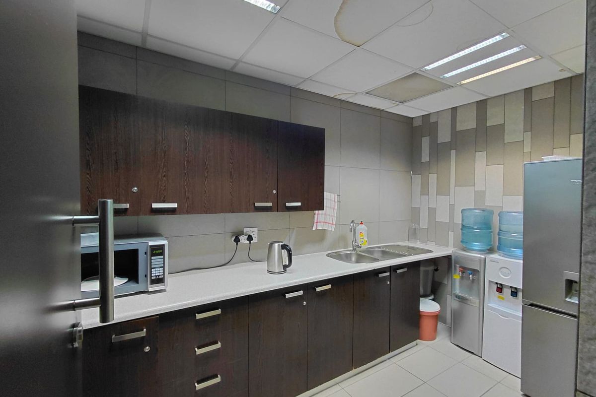 A functional commercial kitchenette featuring dark wood cabinetry, a stainless steel sink, tiled backsplash, and recessed ceiling lighting.
